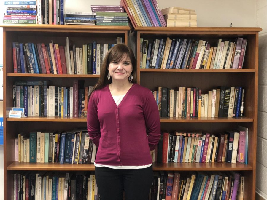 Dr. Heather Rellihan poses in front of a gender studies-themed bookcase outside of her office.