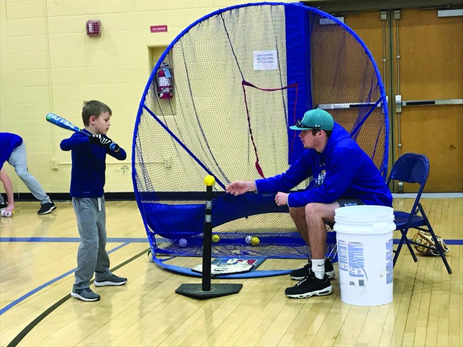 AACC Baseball player John Shupe teaches a youth player how to hit off of a tee.