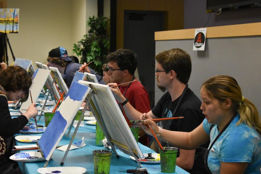 Students paint along with an instructor, creating a fall landscape.