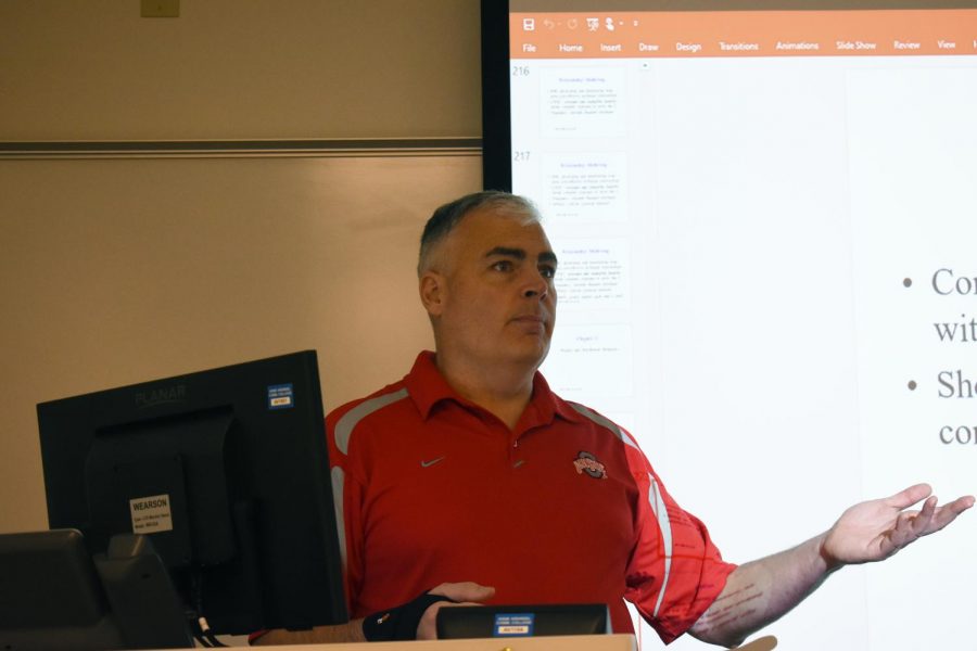 Adjunct business instructor Lou Carloni teaches in front of a projector.