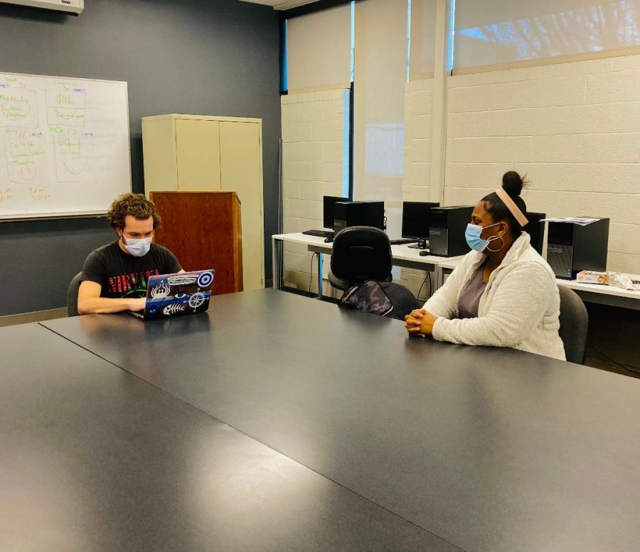 Two students sitting at a large desk in a classroom, wearing masks.