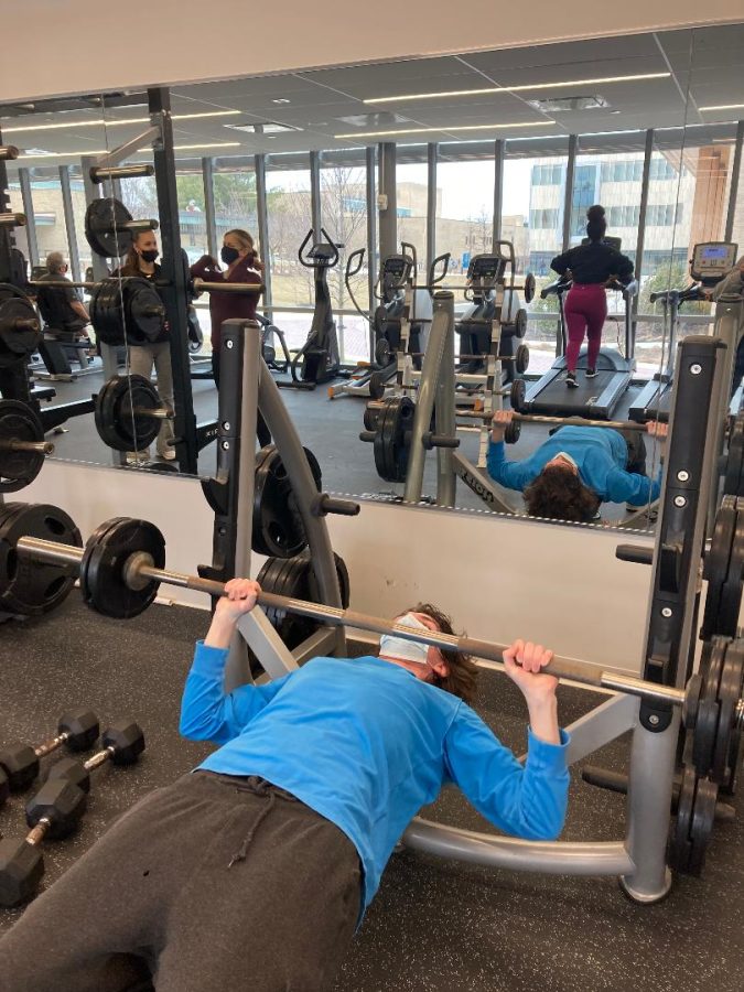 First-year psychology student Austin Smith, who is on AACCs golf team, works out in Jenkins gym. In mirror, womens cross country coach Susan Noble (right) demonstrates the proper use of gym equipment.
