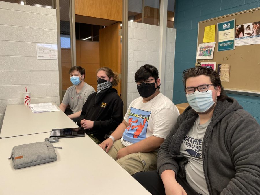 Four male students sit at long desk in an English 102 class