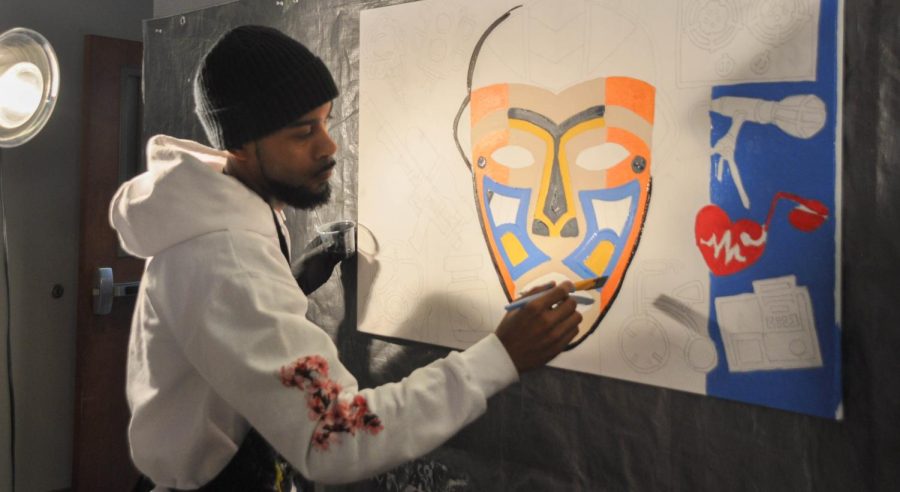 Award-winning Maryland artist Comacell Brown Jr. paints a tribal mask at a Black History Month event. The two canvases were painted by him and AACC students featuring various inventions and products created by black historical figures.